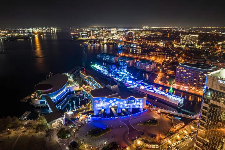 Aerial view of a city waterfront at night with colorful building lights and reflections on water.