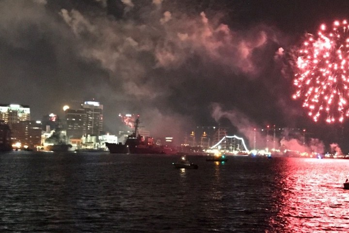 Fireworks over a city skyline at night with reflections on the water.