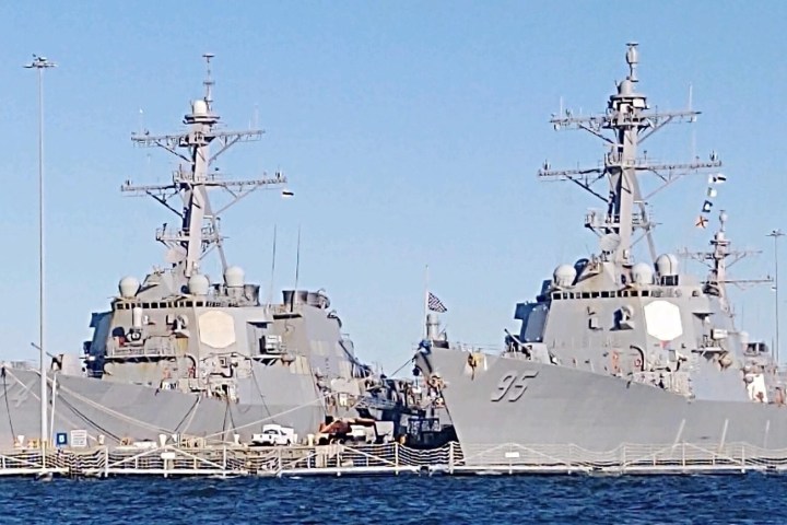 Two gray naval ships docked side by side in a harbor on a clear day.