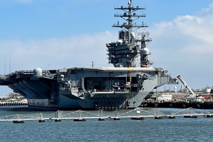 Large aircraft carrier docked at a harbor under a blue sky.