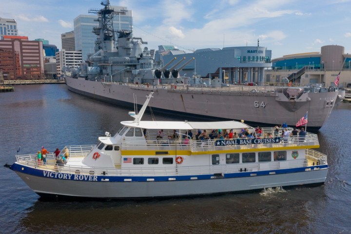 Tour boat Victory Rover in front of large battleship docked in a city harbor.